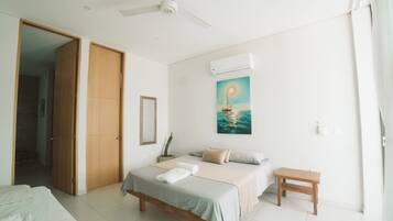 A bedroom with a bed, a bedside table, a ceiling fan, an air conditioning unit, a painting of a sailboat, and a door leading to another room.
