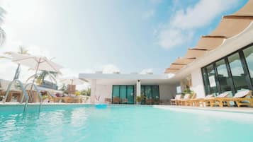 Un espace piscine avec des chaises longues et des parasols, un ciel dégagé et un bâtiment moderne doté de grandes fenêtres.