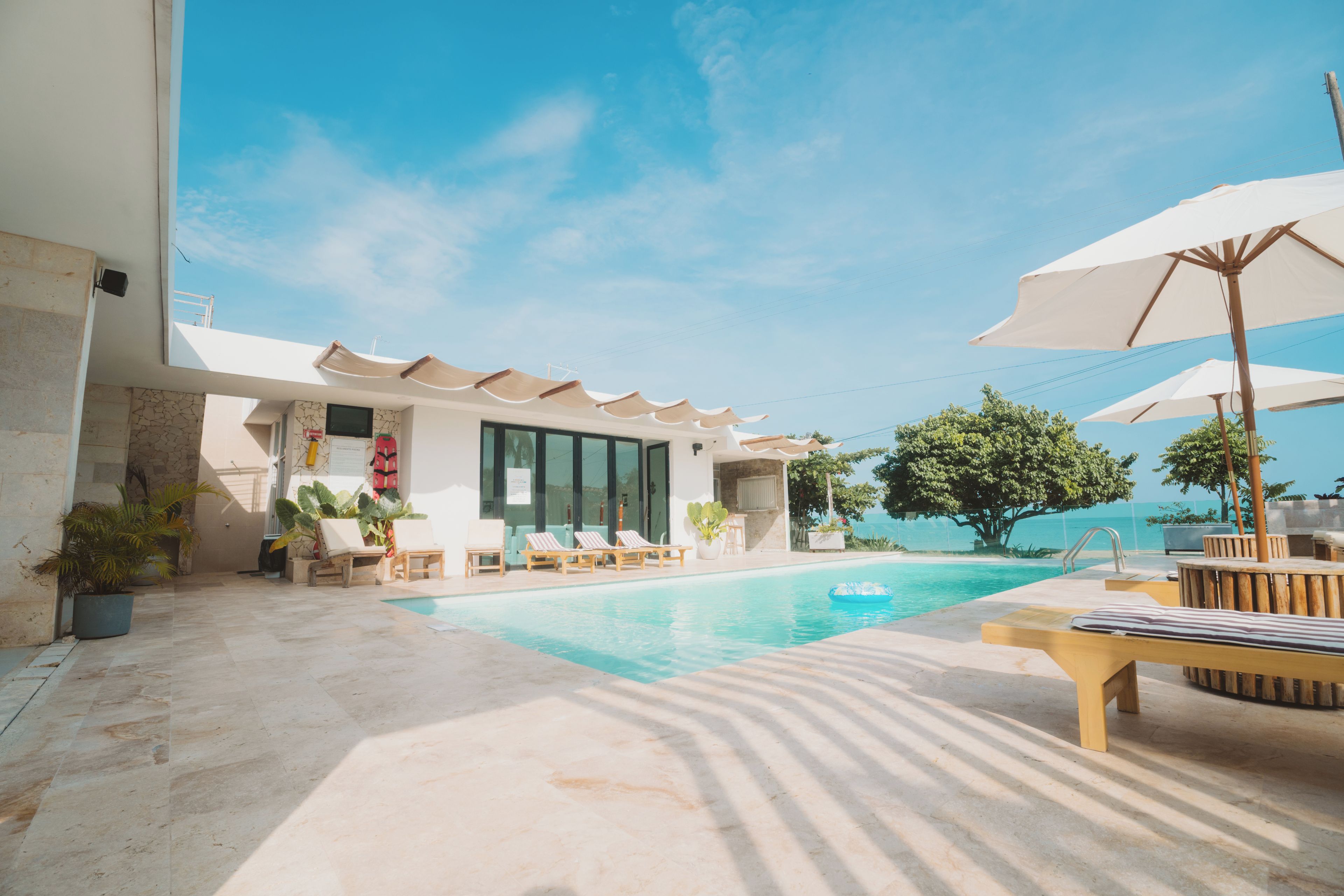 A pool area with lounge chairs and umbrellas, a clear sky, and a view of the sea.