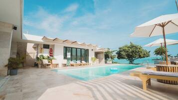 A pool area with lounge chairs and umbrellas, a clear sky, and a view of the sea.