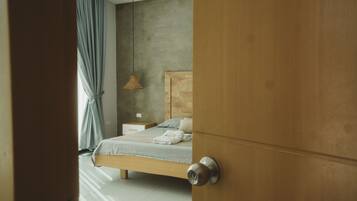 Un dormitorio con puerta de madera, una cama con cabecera, una mesita de noche, una lámpara colgante y una ventana con cortinas.