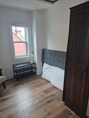 A room with a bed, a wooden floor, a window, a bench, and a wardrobe. - Furnished 3BR Home | All-Inclusive Monthly Vanier (Ottawa)