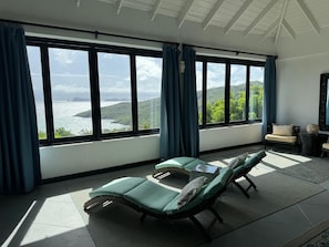 Ein Zimmer mit Blick auf das Meer und die Hügel, ein Bett, ein Sessel und ein kleiner Tisch.