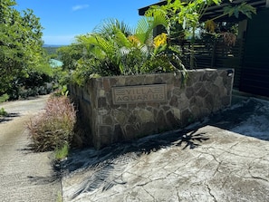Eine Steinsäule mit einem Schild, auf dem 'Villa Aquarius' steht, umgeben von üppigem Grün.