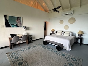 Een slaapkamer met een bed, bureau, stoelen en een plafondventilator.