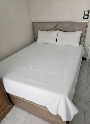 Ein Bett mit Kopfteil, weißer Bettwäsche und Holzboden.