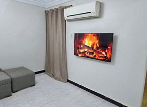 Ein Zimmer mit einem an der Wand befestigten Flachbildfernseher, einem beigen Vorhang und einem grauen Sofa.