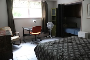Un dormitorio con una cama, un escritorio, una silla, un ventilador de pie y un armario.