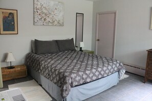 Ein Schlafzimmer mit Bett, Nachttisch, Lampe, einer Tür und einem Bild an der Wand.