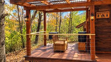 Une terrasse en bois avec un banc et un barbecue, entourée d’arbres aux feuilles d’automne, et un panneau indiquant « Base camp de Roses Brook ».