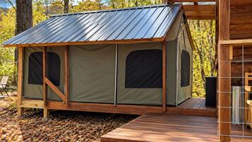 Une cabane en bois avec un toit en métal, une terrasse et une structure ressemblant à une tente, dotée de fenêtres.