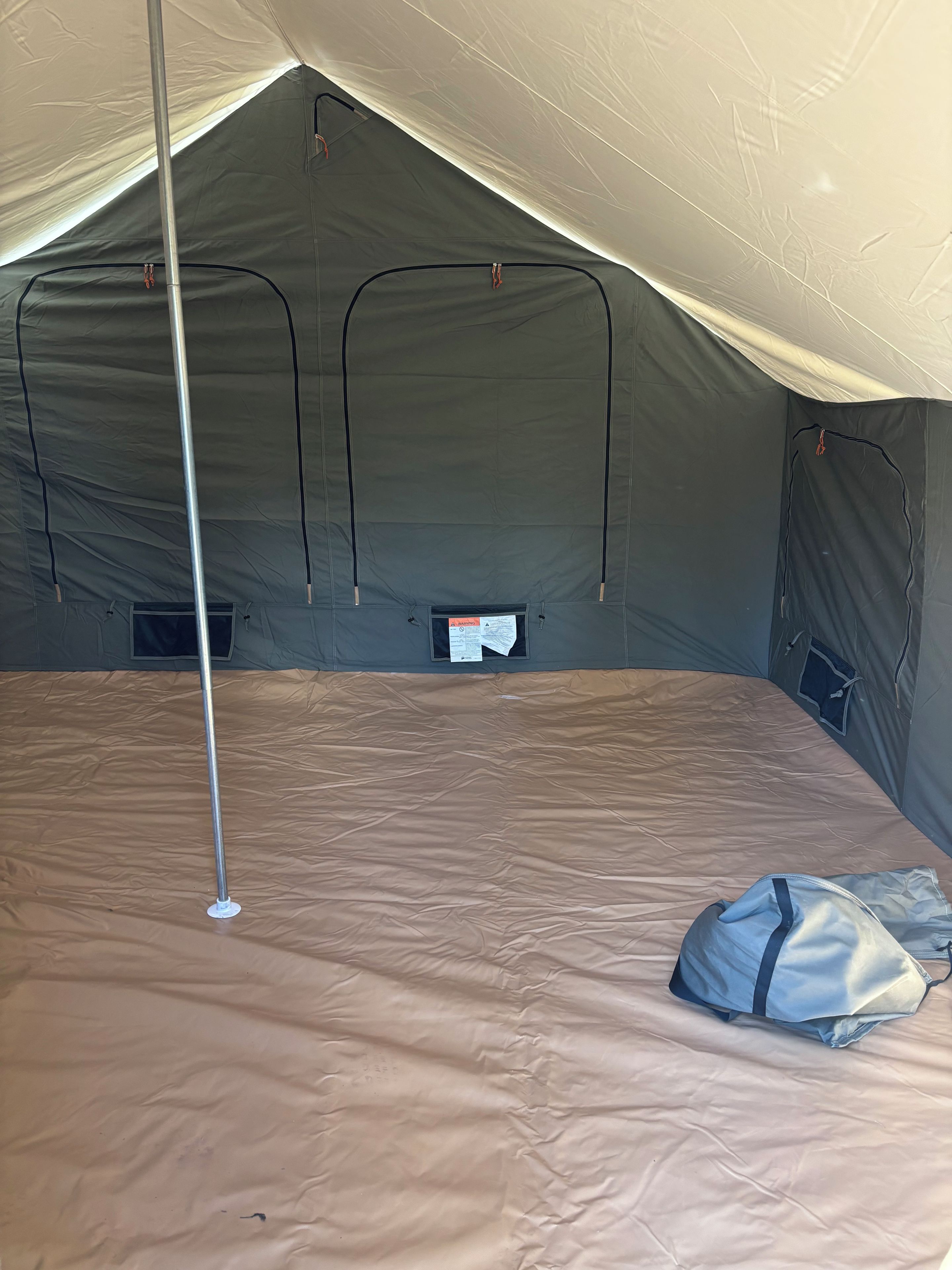Une tente avec un poteau central, un sac de couchage et un sac posé sur le sol.