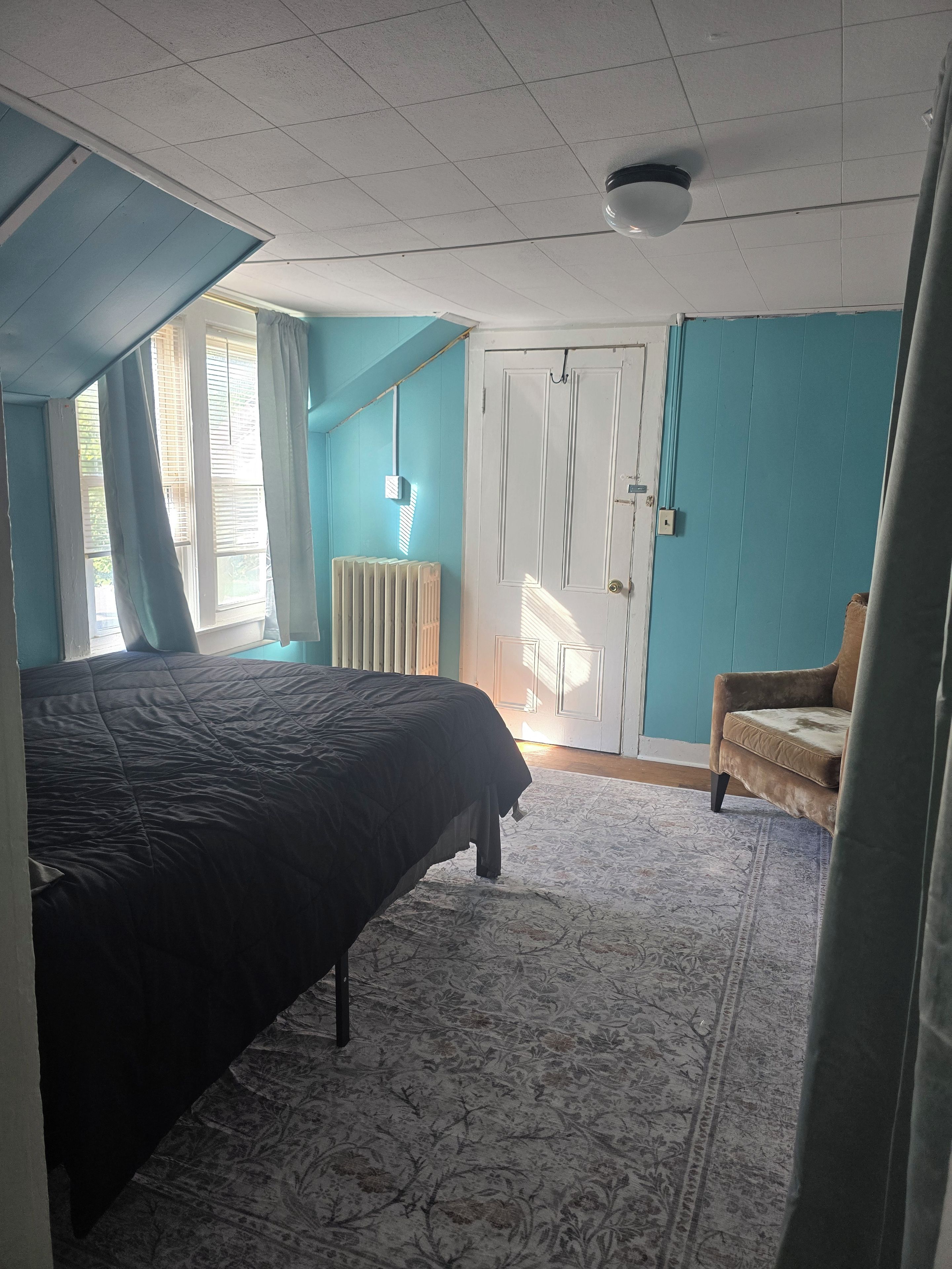 A bedroom with a bed, a chair, a radiator, and a door.