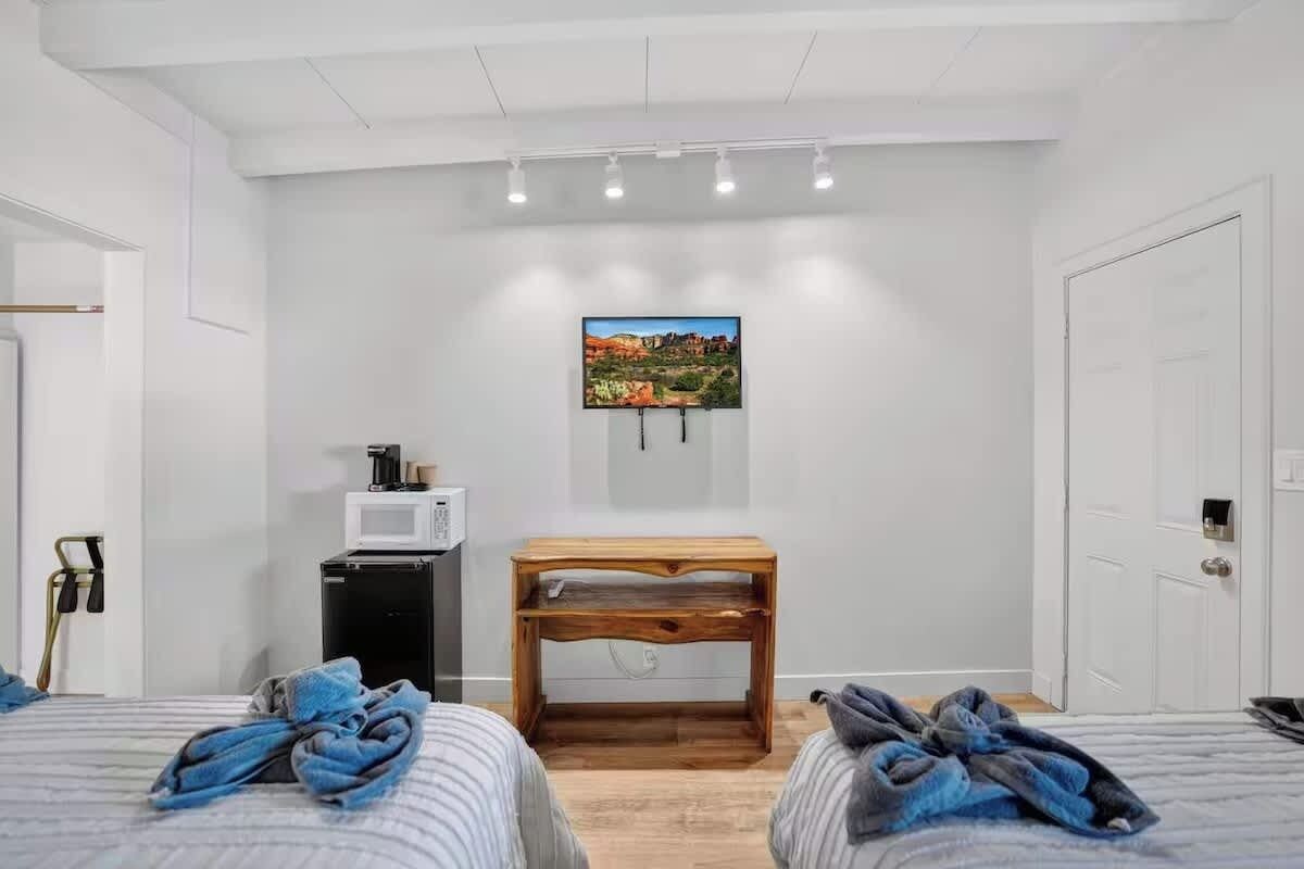 Una habitación de hotel con dos camas, una mesita de noche de madera, un televisor montado en la pared y una puerta.
