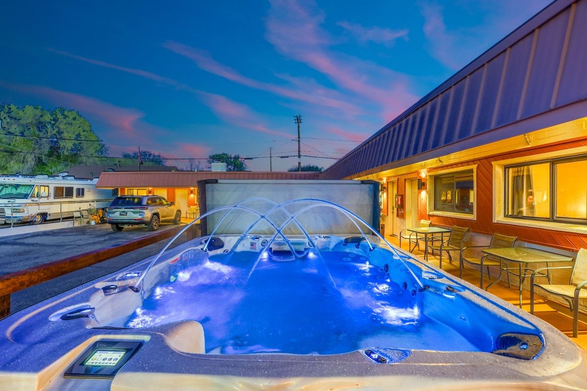 A hot tub with a control panel, surrounded by outdoor seating and a building with large windows.