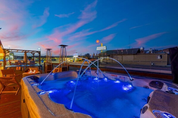 A hot tub with a view of a restaurant and a city skyline at dusk.