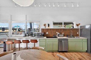 A modern kitchen with a large island, green cabinets, and a view of the street.