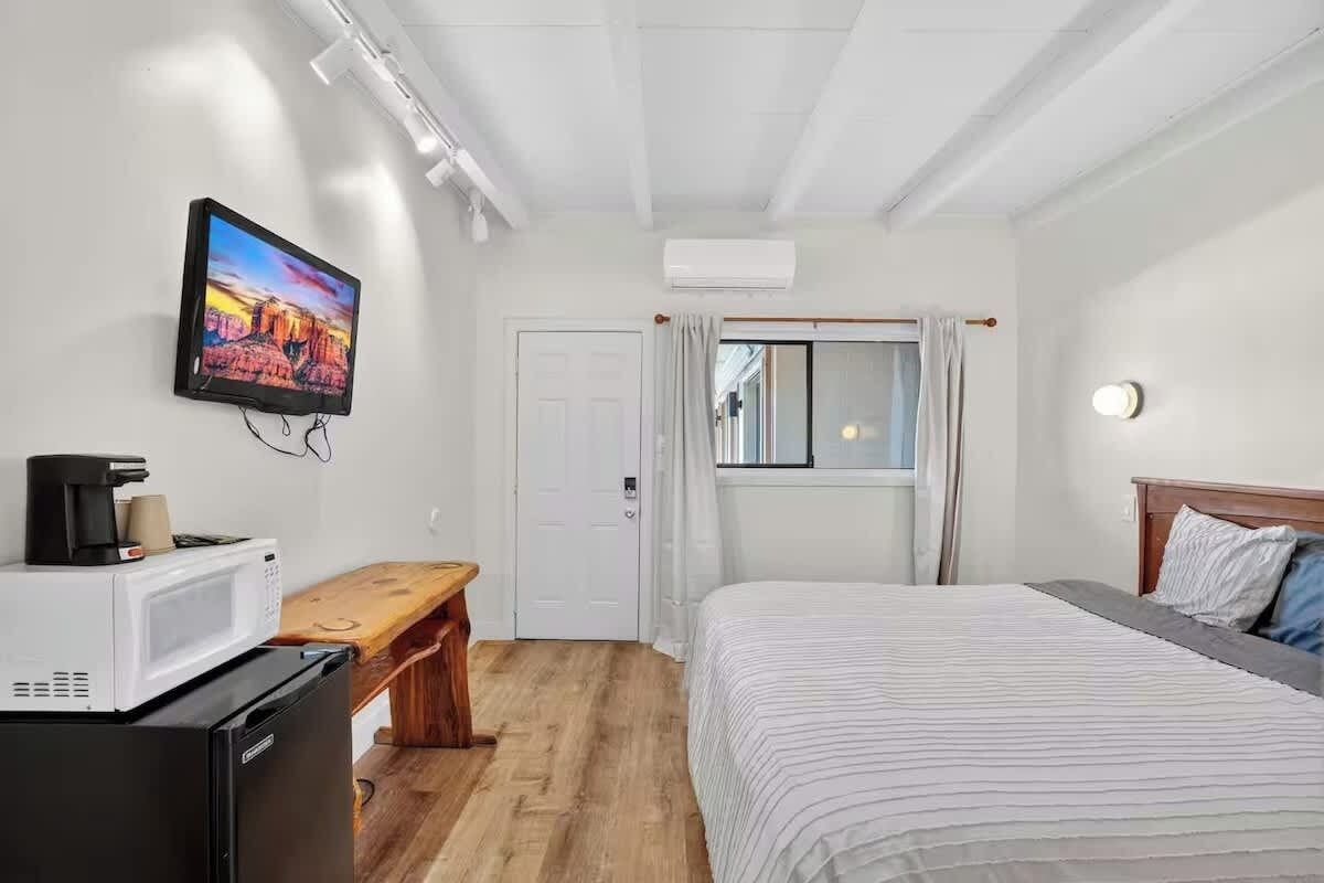 Ein Hotelzimmer mit einem Bett, einem Schreibtisch mit Mikrowelle, einem an der Wand befestigten Fernseher und einem Fenster mit Vorhängen.