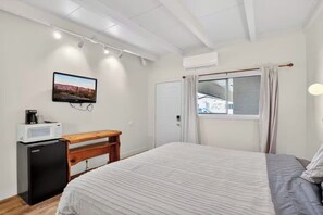 A bedroom with a bed, a desk, a television, a microwave, and an air conditioner. - Highlander Room 7 Private Room near Route 66 (Williams)