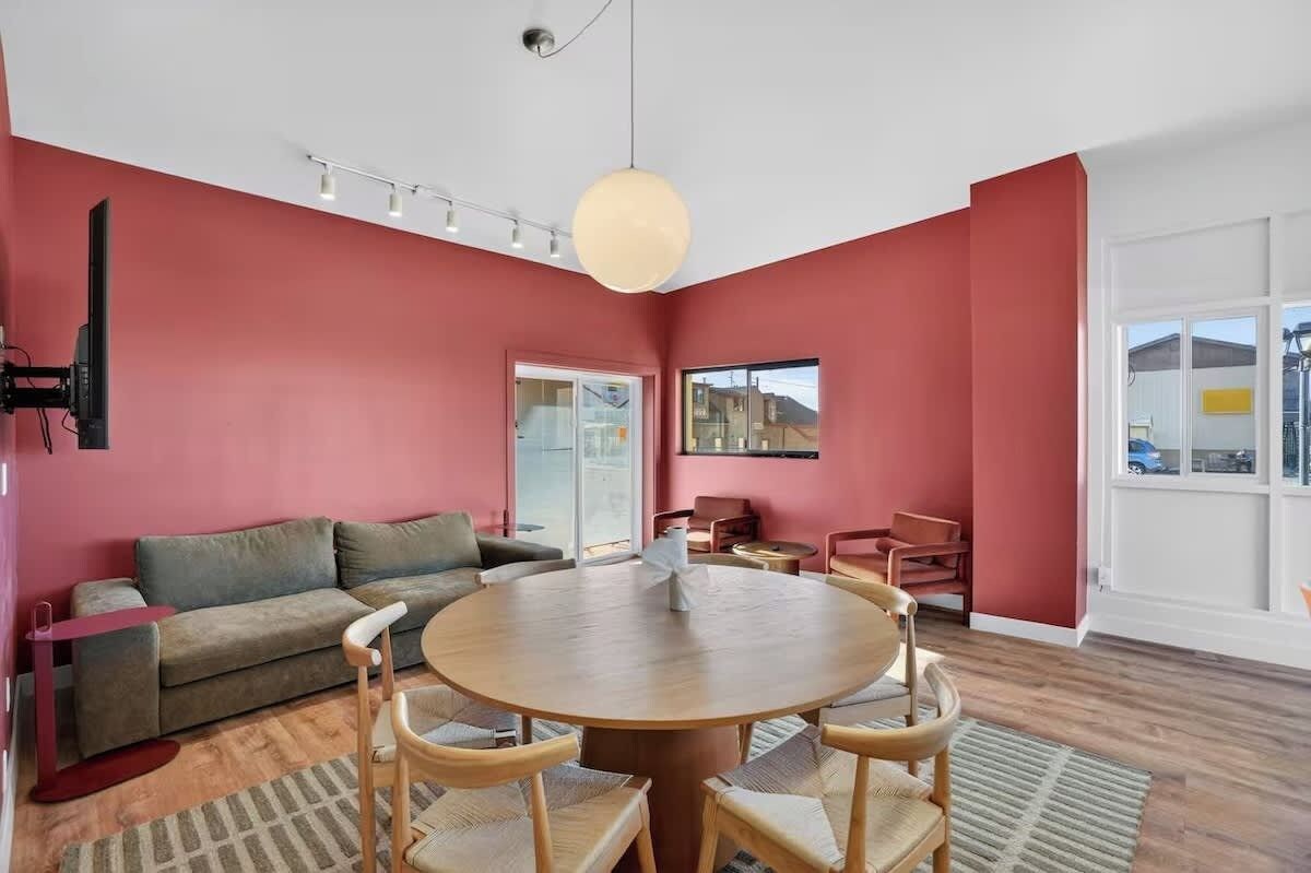 Una sala de estar moderna con una mesa redonda de madera, un sofá gris y una pared de acento roja.