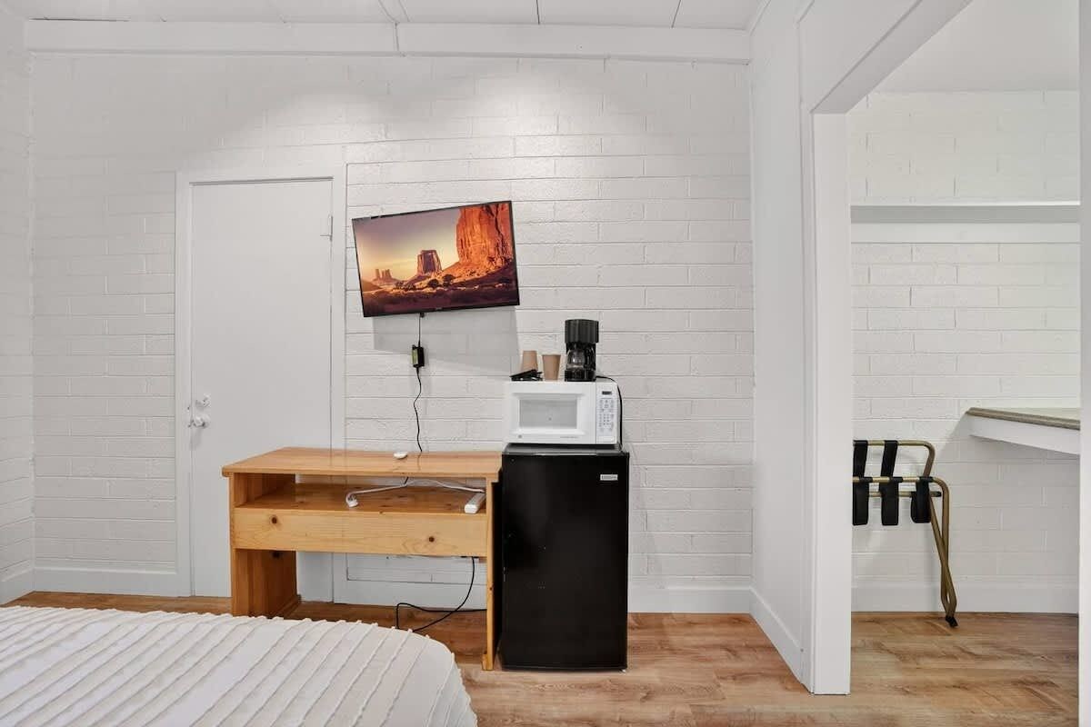 A compact room with a bed, a desk with a computer, a TV mounted on the wall, a microwave, and a refrigerator.