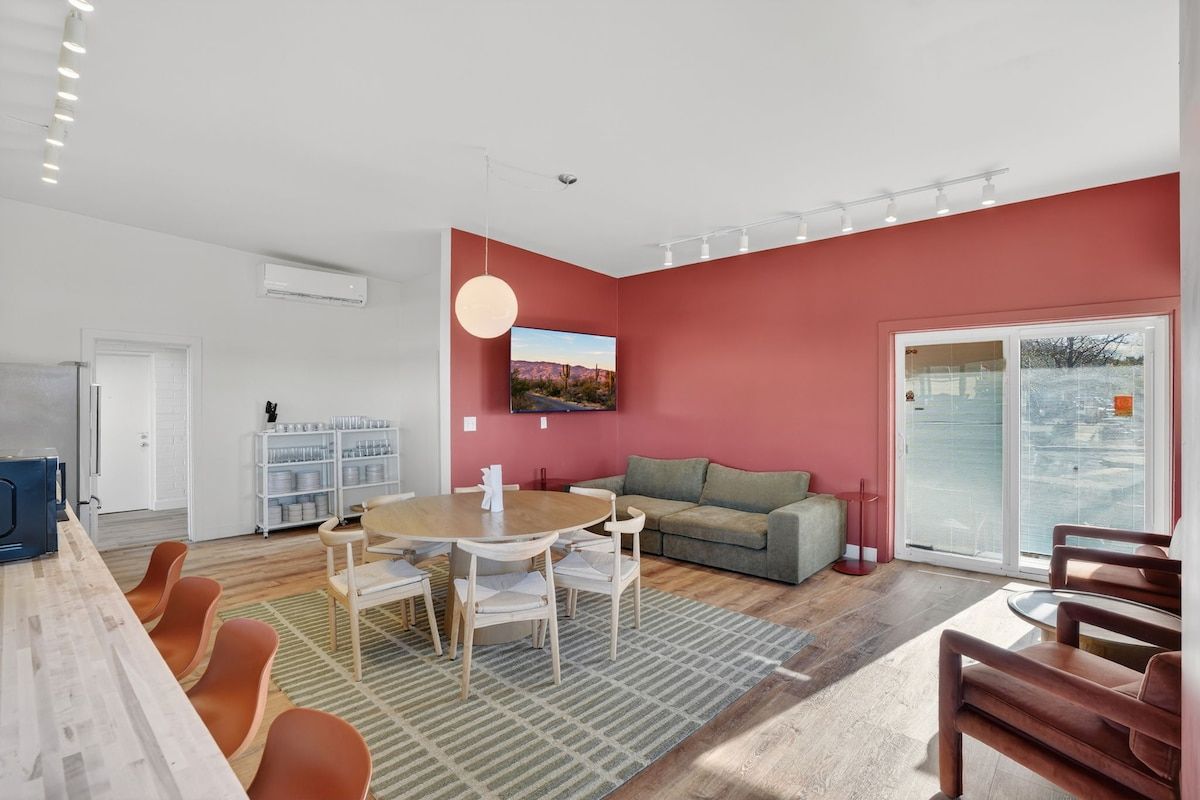 A modern living room with a red accent wall, a round dining table, and a sofa.
