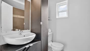 Une salle de bain avec un lavabo blanc, un miroir, des toilettes et une fenêtre.