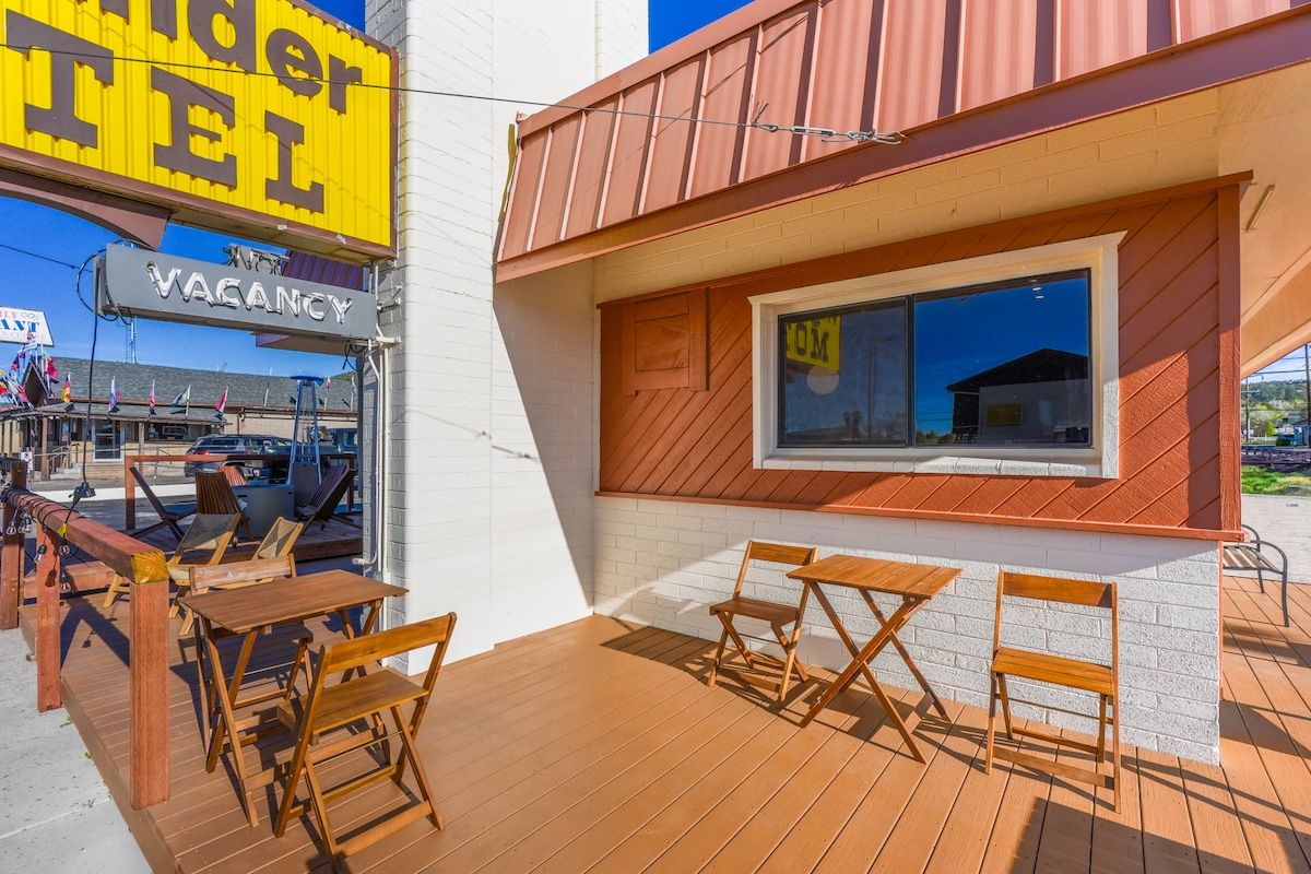 A hotel exterior with a wooden deck, outdoor seating, and a visible window.