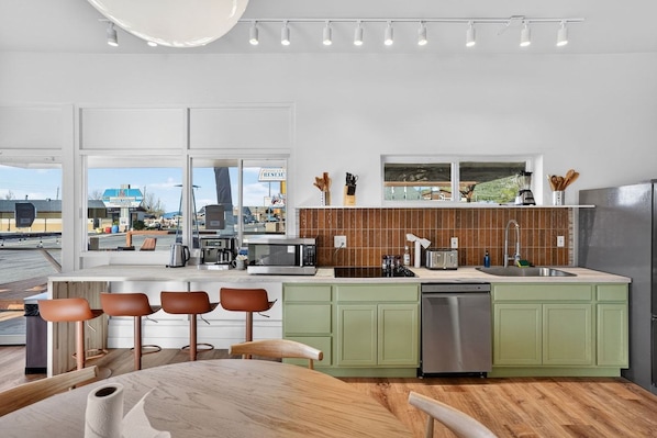 A modern kitchen with a large island, green cabinets, and a view of the street.