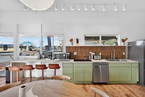 Een moderne keuken met een groot eiland, groene kastjes en uitzicht op de straat.