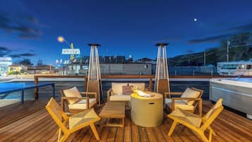 A deck with outdoor seating and a fire feature, overlooking a marina with boats and a restaurant sign.