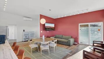 A modern living room with a dining area, a sofa, and a television mounted on the wall.