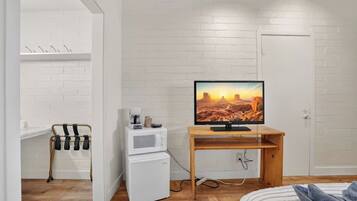 Een kamer met een witte bakstenen muur, een houten tafel met een televisie, een witte koelkast en een bed met een gestreepte deken.