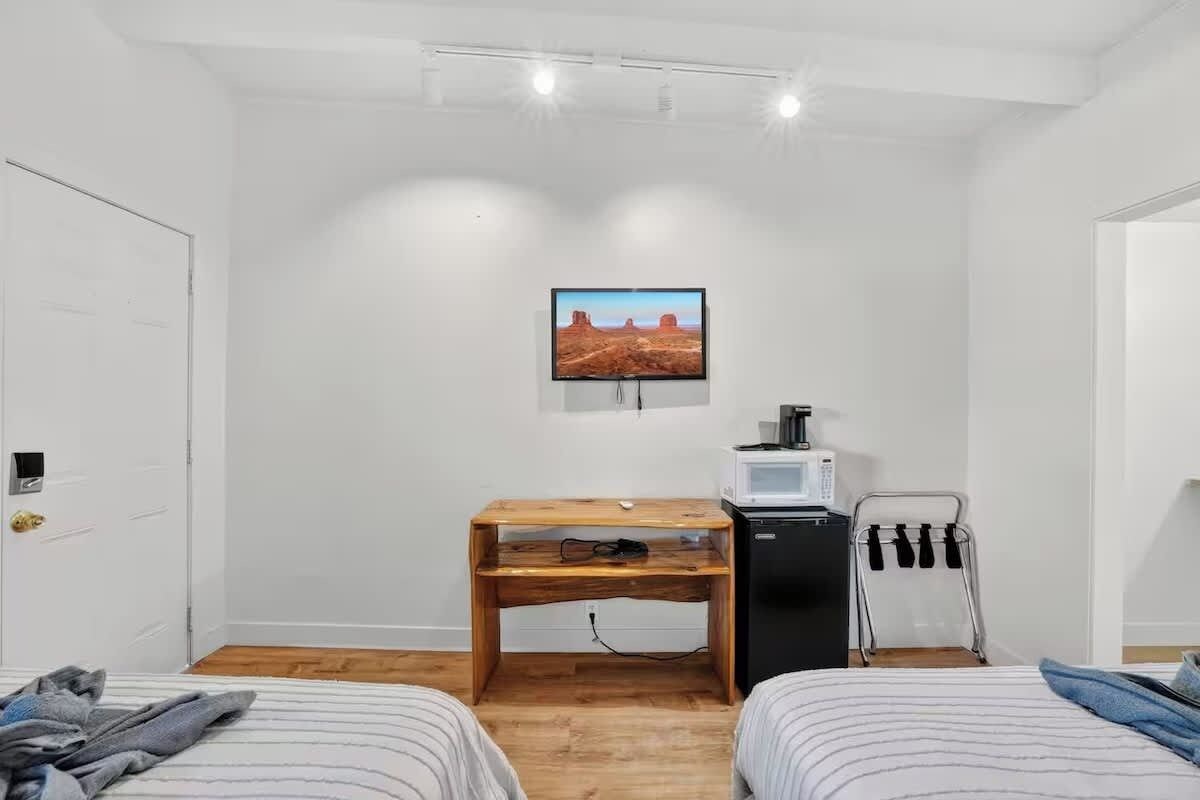 A room with two beds, a wooden desk, a television, a microwave, and a towel rack.