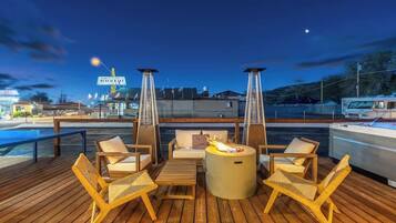 A deck with outdoor seating and a fire feature, overlooking a marina with boats and a restaurant sign.