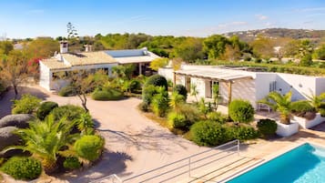 A modern villa with a swimming pool, surrounded by lush greenery and a clear sky.
