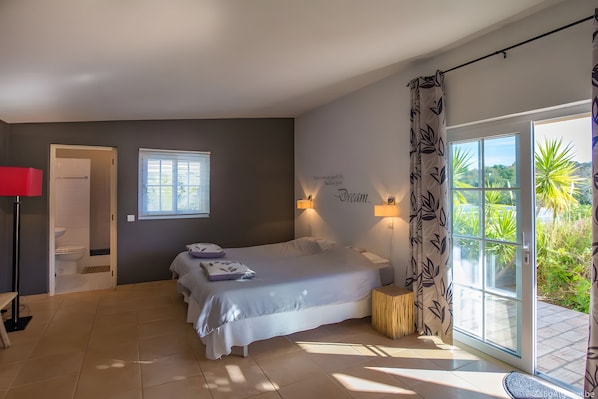 A bedroom with a bed, a window with blinds, a door, and a view of greenery outside. - Villa 'Casa Caranguejo' with Private Pool (Loulé)