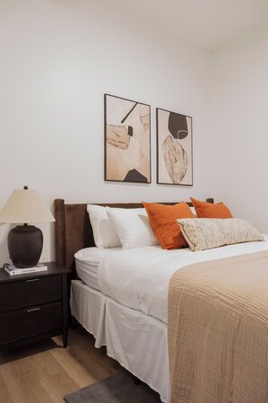 A bedroom with a bed, pillows, a nightstand, a lamp, and two wall art pieces. - Designer Combo Loft 3E & 3W|GoldCoast/River North (Chicago)