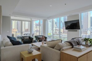 A modern living room with a city view, a flat-screen TV mounted on the wall, and a comfortable seating area with sofas and a coffee table. - Luxury Loft Collection COMBO 901/903 | Terrace (Chicago)