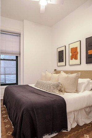 A bedroom with a bed, a window with blinds, and three framed artworks on the wall. - Designer Combo Loft 4E & 4W|Gold Coast/River North (Chicago)