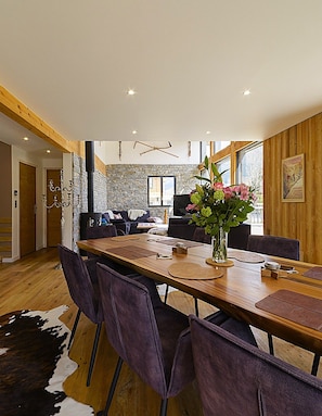 Ein moderner Essbereich mit einem langen Holztisch, violetten Stühlen und einer Blumenvase.