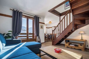 A cozy living room with a blue sofa, wooden table, and a staircase leading to a dining area.