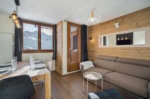 A modern interior with a wooden wall, a sofa, a dining table set, and a view of mountains.