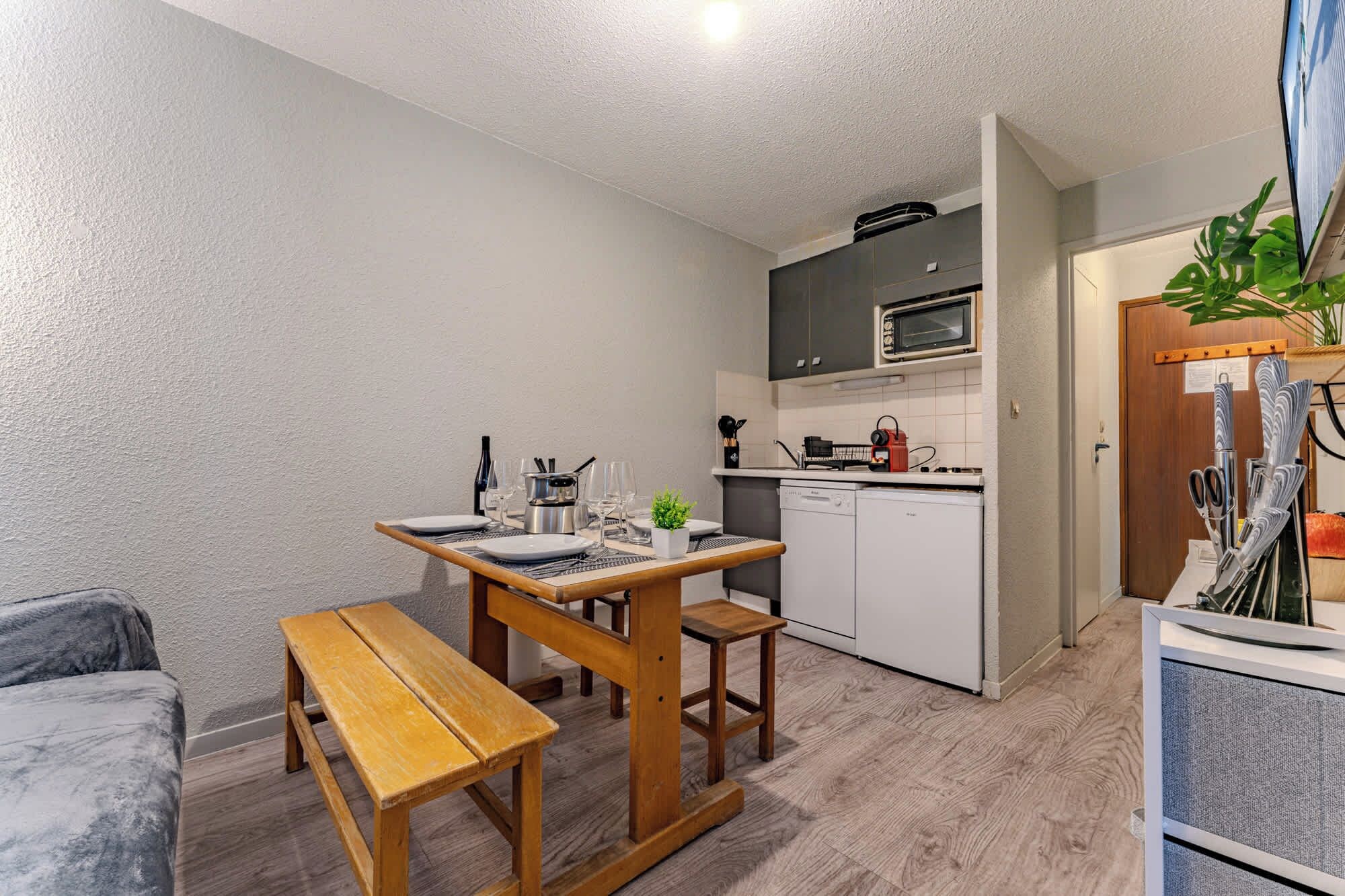 A compact kitchen with a microwave, stove, and dishwasher. A wooden bench and table are set up for dining.