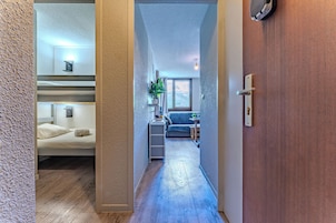 A narrow hallway leading to a bedroom with bunk beds, a small kitchenette, and a living area with a sofa and a plant.