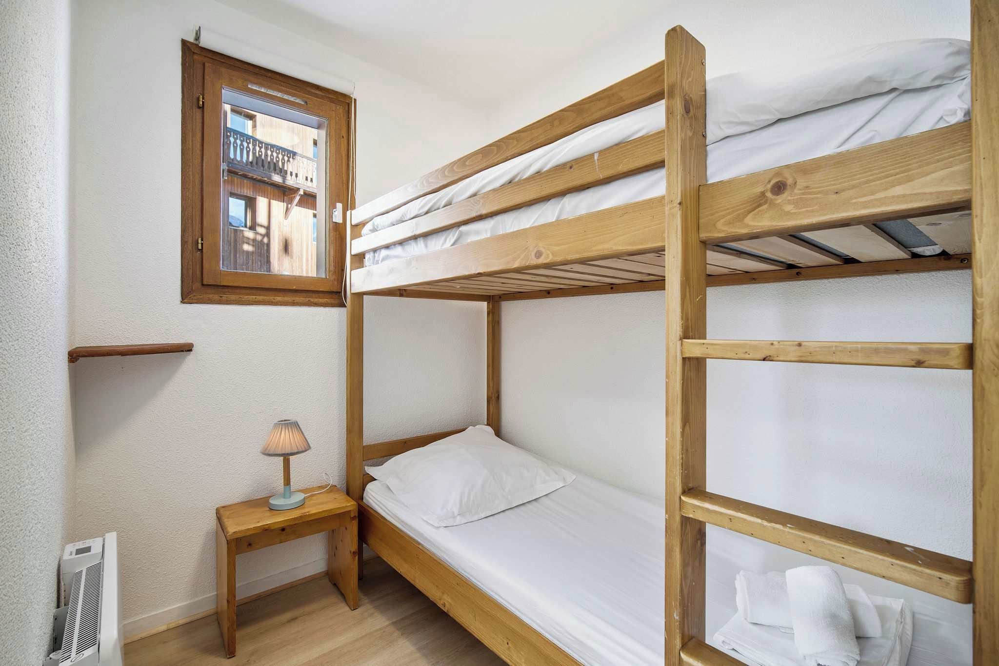 Une chambre avec un lit superposé, une fenêtre, une table de chevet avec une lampe et un radiateur.
