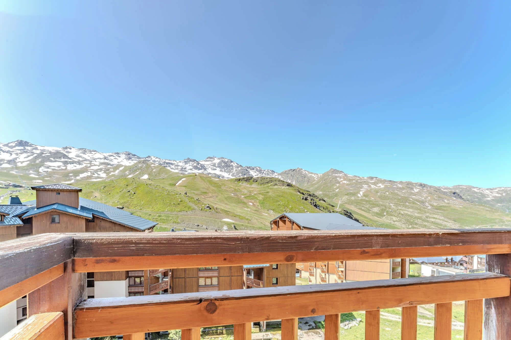A wooden balcony with a view of snow-capped mountains and a clear sky.