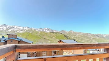 A wooden balcony with a view of snow-capped mountains and a clear sky.
