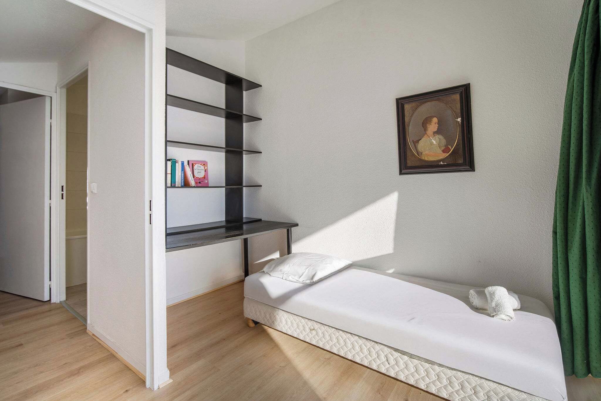 Un dormitorio con cama, estantería, cuadro enmarco y cortina verde.