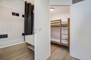 A small, compact room with a wooden bunk bed, a white sink, and a shower area with a curtain.